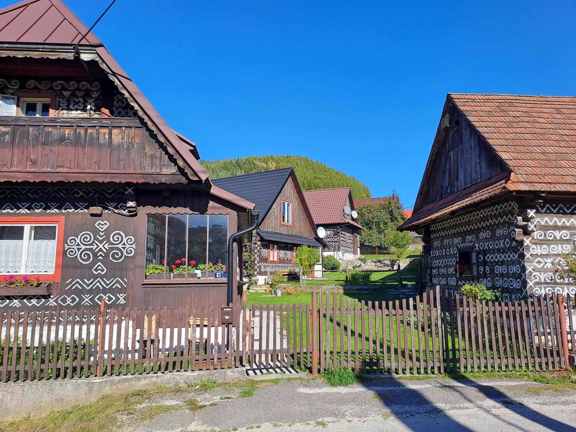 Pohled do jedné z uliček památkové rezervace lidové architektury s malovanými dřevěnicemi a hřebenem Strážovských vrchů v pozadí. Foto: Se svolením Petra Kučery